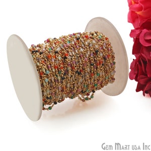 May include: A spool of gold chain with colorful gemstone beads. The chain is wound around a white spool. The chain is made of gold-plated metal and the beads are made of various gemstones, including amethyst, citrine, and garnet.