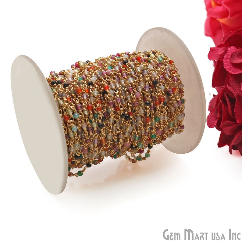 May include: A spool of gold chain with colorful gemstone beads. The chain is wound around a white spool. The chain is made of gold-plated metal and the beads are made of various gemstones, including amethyst, citrine, and garnet.