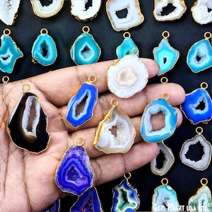 May include: Assortment of agate gemstone pendants with gold-plated bail. The pendants are various shapes and sizes, with a variety of colors including blue, black, white, and purple.