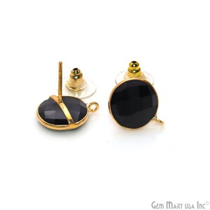 May include: A pair of black faceted gemstone stud earrings with gold-colored settings. The earrings have a round shape and a small loop for attaching additional charms or dangles. The posts are gold-colored with clear earring backs.