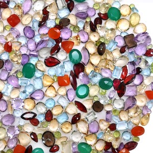 Può includere: Una vasta collezione di pietre preziose sfaccettate sciolte di varie forme e dimensioni, inclusi tagli rotondi, ovali, a goccia, quadrati e marquise. Le pietre presentano una tavolozza di colori variegata in tonalità rosse, verdi, viola, azzurre, gialle e trasparenti.
