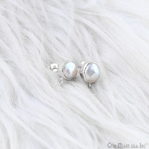May include: A pair of pearl stud earrings. Each earring features a lustrous, off-white, baroque pearl set in a silver bezel. The earrings are displayed on a white, fluffy surface.