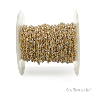 Könnte beinhalten: Eine Spule mit goldfarbener Kette mit grauen Edelsteinperlen. Die Kette ist um eine transparente Kunststoffspule gewickelt.