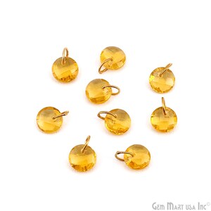 May include: A collection of round, faceted, golden-yellow gemstone charms with small gold-colored loops for jewelry making. The charms are scattered on a white background, showcasing their sparkling facets and warm color.