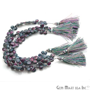 May include: A strand of faceted ruby beads with a deep red and blue color. The beads are strung on a silver wire and have a tassel at each end. The tassels are made of green, purple, and pink threads.
