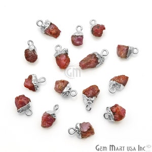May include: A collection of 15 raw ruby gemstone pendants with silver-toned jump rings. The ruby gemstones are a deep red color and have a rough, natural texture.