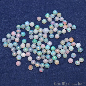May include: A collection of white opal cabochons with iridescent rainbow flashes. The cabochons are round and have a smooth, polished surface. They are scattered on a blue background.
