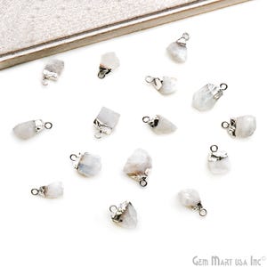 May include: A collection of small, raw moonstone pendants with silver-colored metal caps and loops. The pendants are irregularly shaped and vary in size, with a milky white color. They are scattered on a white surface.