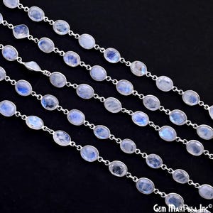 May include: A strand of silver chain with oval-shaped moonstone beads. The chain is shown in multiple rows, highlighting the iridescent quality of the moonstone.