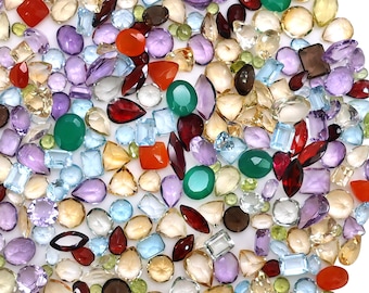 May include: A large collection of loose, faceted gemstones in various shapes and sizes, including round, oval, pear, square, and marquise cuts. The stones feature a diverse color palette of red, green, purple, light blue, yellow, and clear tones.