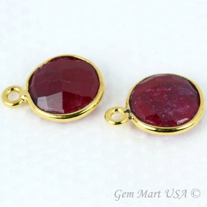 May include: Two gold-plated round pendants with red ruby gemstones. Each pendant has a small loop for attaching to a chain or cord.