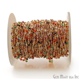 May include: A spool of gold chain with small, colorful gemstone beads. The chain is made of gold-plated metal and the beads are a mix of red, green, blue, and purple.