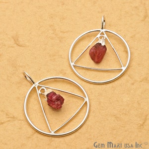 May include: Two silver pendants with a triangle design and a red gemstone hanging inside. The pendants are on a brown background.