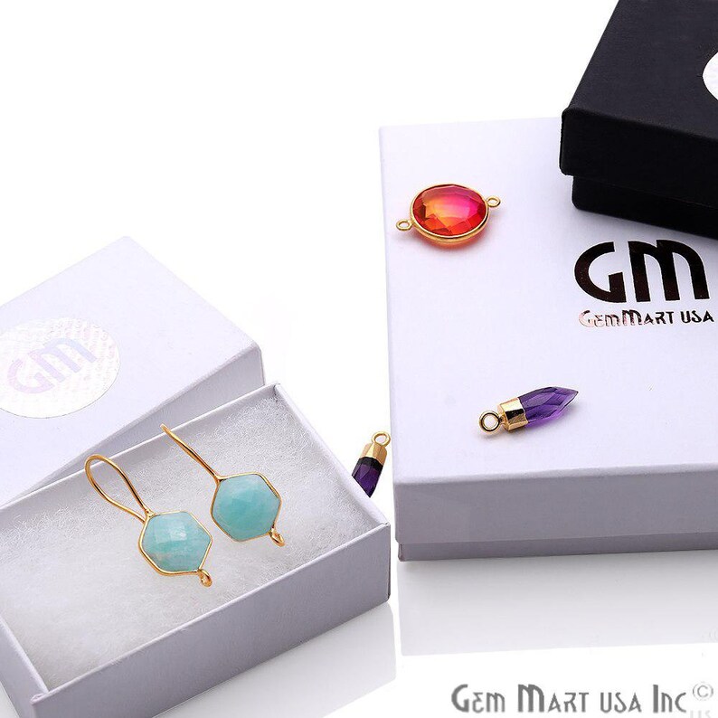 May include: Two pairs of gold-plated earrings with light blue gemstone accents. The earrings are displayed in a white box with the Gem Mart USA logo.
