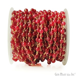 May include: A spool of red gemstone beads strung on a gold chain. The beads are round and have a smooth, polished finish.