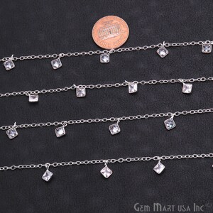 K&ouml;nnte beinhalten: Vier Str&auml;nge silberner Kette mit baumelnden quadratischen, klaren Kristallen. Die Ketten sind versetzt angeordnet, wobei die oberste Kette die meisten Kristalle und die unterste Kette die wenigsten Kristalle hat. Ein US-Penny ist zur Gr&ouml;&szlig;enbestimmung enthalten.