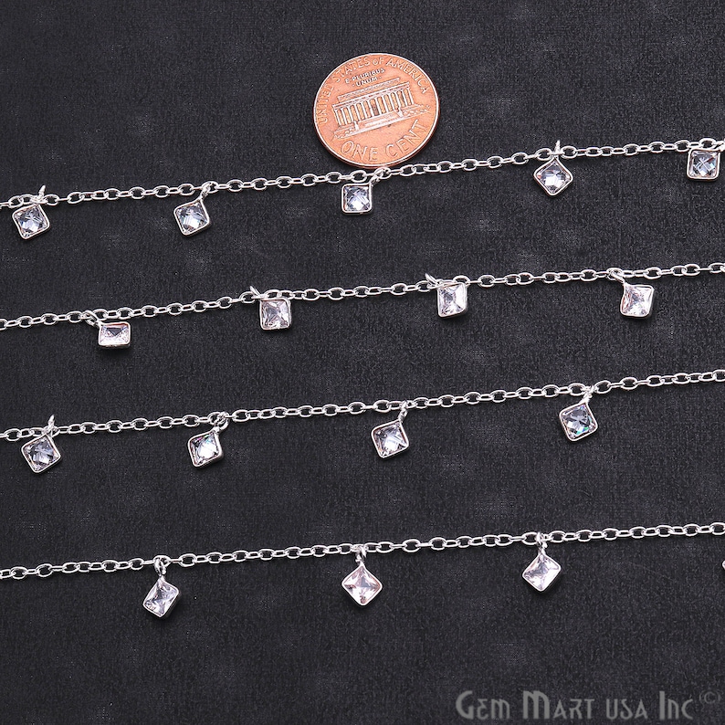 K&ouml;nnte beinhalten: Vier Str&auml;nge silberner Kette mit baumelnden quadratischen, klaren Kristallen. Die Ketten sind versetzt angeordnet, wobei die oberste Kette die meisten Kristalle und die unterste Kette die wenigsten Kristalle hat. Ein US-Penny ist zur Gr&ouml;&szlig;enbestimmung enthalten.