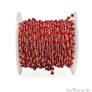 May include: A spool of red gemstone beads strung on a gold chain. The beads are faceted and have a shiny finish. The chain is delicate and has a gold color.