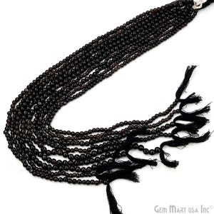 May include: Strands of dark brown gemstone beads with a glossy finish. Each strand is composed of small, round beads. Black tassels are attached at the bottom. The beads are likely used for jewelry making.