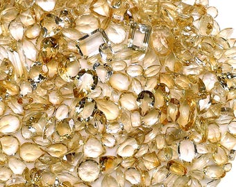 May include: A large collection of loose, faceted gemstones in various shapes including pear, oval, round, and rectangular cuts. The stones exhibit a range of yellow and golden hues, varying from pale translucent shades to deeper amber tones.