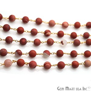 May include: A strand of red jasper beads with gold wire accents. The beads are round and have a natural, speckled appearance.