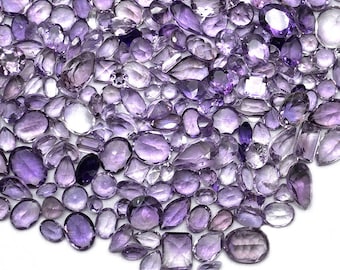 May include: A large collection of amethyst gemstones in various shapes and sizes, including oval, round, pear, and rectangular cuts. The stones are a light to medium purple color and have a smooth, polished finish.