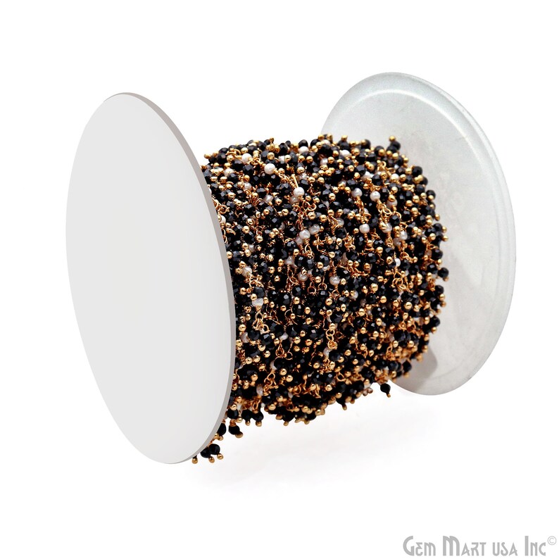 K&ouml;nnte beinhalten: Eine Spule mit Perlenkette mit schwarzen und wei&szlig;en Perlen auf goldfarbenem Draht. Die kleinen Perlen sind gleichm&auml;&szlig;ig verteilt und bilden ein filigranes Muster. Die wei&szlig;e Spule bietet einen sauberen Hintergrund f&uuml;r die Kette und hebt das Design hervor.