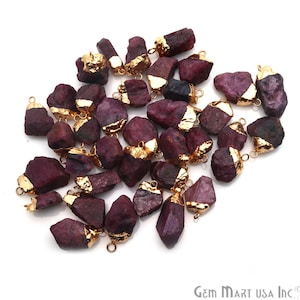May include: A collection of 25 raw ruby gemstone pendants with gold-plated jump rings. The ruby stones are a deep red color and have a natural, rough texture. The gold jump rings are attached to the top of each stone.
