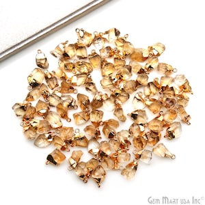 May include: A large group of gold-toned raw citrine gemstone pendants with jump rings. The citrine stones are irregular in shape and have a light brown color.