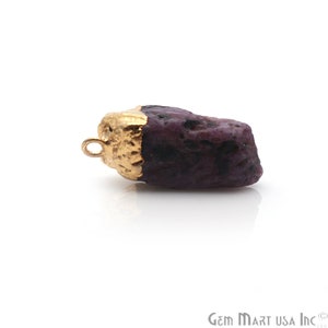 May include: A raw ruby gemstone pendant with a gold-plated setting. The ruby is a deep purple color and has a rough, natural texture. The pendant is ready to be strung on a necklace or bracelet.