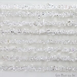 May include: A strand of clear quartz chip beads, arranged in rows on a white background. The beads are small and irregular in shape, with a natural, unpolished finish.