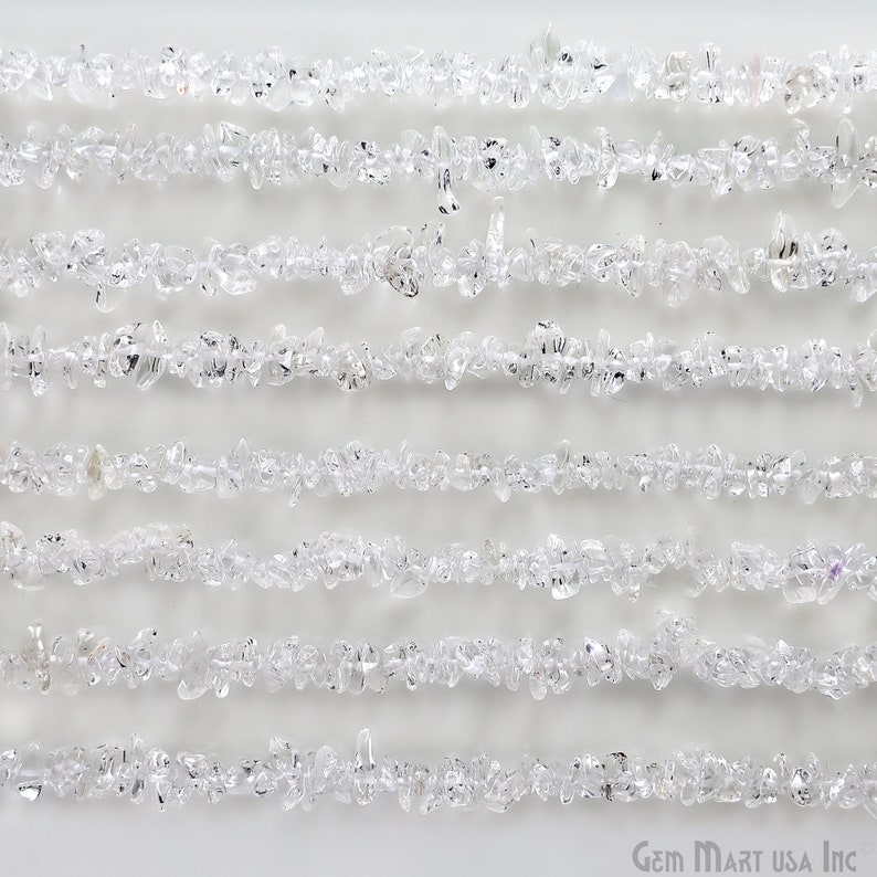 May include: A strand of clear quartz chip beads, arranged in rows on a white background. The beads are small and irregular in shape, with a natural, unpolished finish.