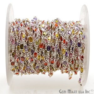 May include: A spool of silver chain with colorful oval-shaped gemstones. The chain is made of silver and has a variety of colors, including red, yellow, green, purple, and pink.