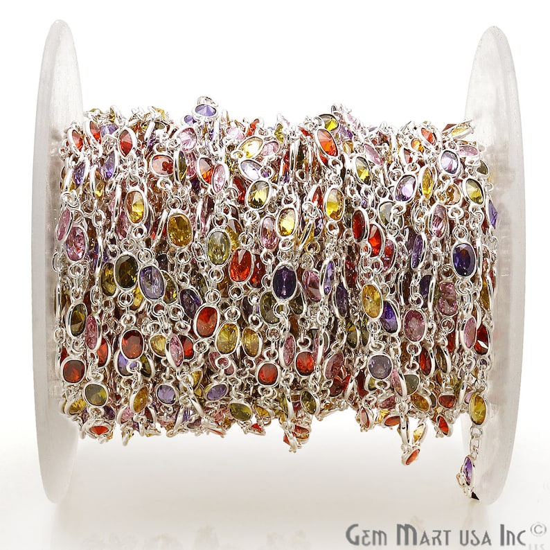 May include: A spool of silver chain with colorful oval-shaped gemstones. The chain is made of silver and has a variety of colors, including red, yellow, green, purple, and pink.