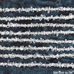 May include: A strand of clear quartz chip beads, arranged in rows on a dark blue background. The beads are small and irregular in shape, with a natural, unpolished finish.
