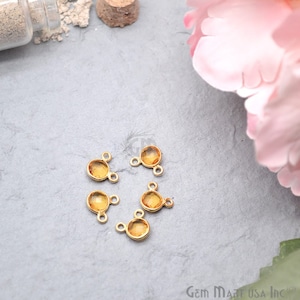 May include: Six gold-toned metal connector charms with a round, clear, amber-colored gemstone in the centre. Each charm has two loops on the side.