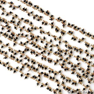 K&ouml;nnte beinhalten: Nahaufnahme mehrerer Str&auml;nge von Perlenschmuck. Die Str&auml;nge weisen kleine, runde schwarze und wei&szlig;e Perlen auf, die auf goldfarbenem Draht aufgef&auml;delt sind. Die Perlen sind in einem sich wiederholenden Muster angeordnet, wodurch ein zartes und kompliziertes Design entsteht.