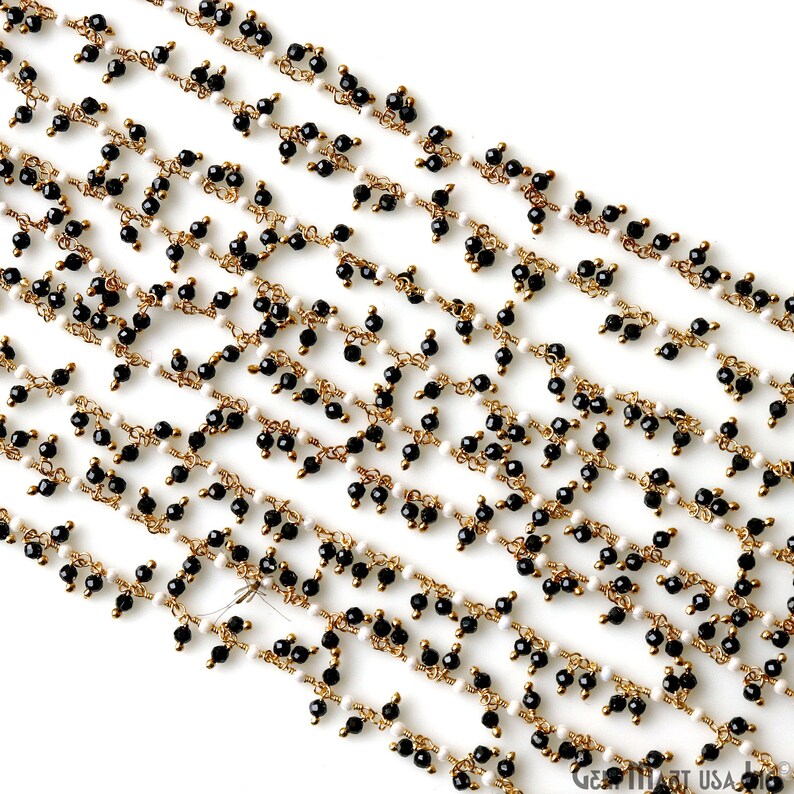 K&ouml;nnte beinhalten: Nahaufnahme mehrerer Str&auml;nge von Perlenschmuck. Die Str&auml;nge weisen kleine, runde schwarze und wei&szlig;e Perlen auf, die auf goldfarbenem Draht aufgef&auml;delt sind. Die Perlen sind in einem sich wiederholenden Muster angeordnet, wodurch ein zartes und kompliziertes Design entsteht.