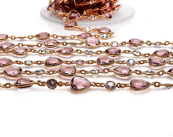 May include: A gold chain with alternating clear and pink faceted glass beads. The chain is laid out in a straight line on a white surface.