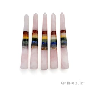 May include: Five vertical rose quartz crystal wands, each featuring a pointed top and a series of seven horizontal bands of colored stones in red, orange, yellow, green, blue, indigo, and violet, arranged in a stack against a white background.
