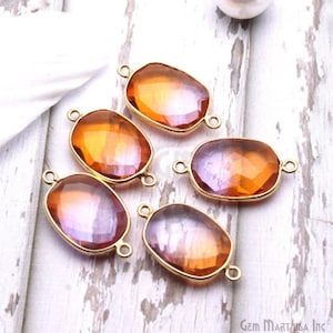 May include: Five faceted, oval-shaped gemstone pendants with gold-colored metal frames. The gemstones transition from orange to purple hues. Each pendant has two loops for attaching to jewelry. The background is a light wood grain.