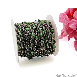 May include: A spool of green and purple gemstone beads strung on a silver chain. The chain is used for making jewelry.