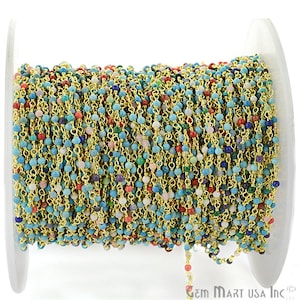 May include: A spool of gold chain with small, colourful gemstone beads. The chain is made of gold-plated metal and the beads are a mix of turquoise, pink, red, green, and blue.