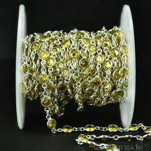 May include: A spool of silver chain with yellow round glass beads. The chain is wound around a white spool.