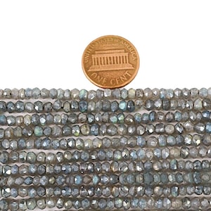 May include: A strand of gray faceted labradorite beads, approximately 4mm in size, with iridescent flashes of color. The beads are shown next to a US penny for scale.