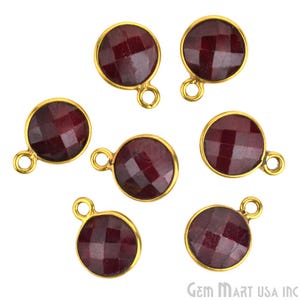 May include: Seven gold-toned pendants with red gemstone round cabochons. Each pendant has a loop for attaching to a chain or cord.