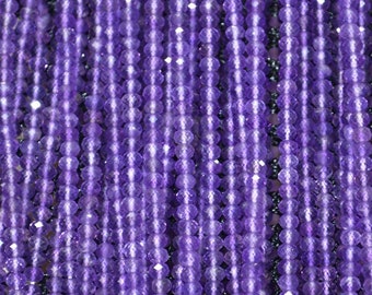 May include: A close-up view of a strand of amethyst beads. The beads are faceted and have a deep purple color. The beads are strung on a clear thread.