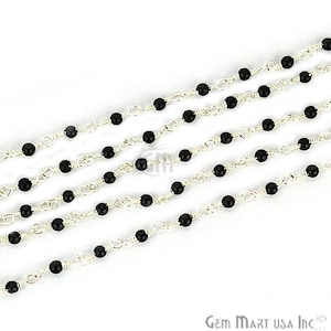 May include: Black beads strung on a silver chain. The chain is made of small, linked circles. The beads are evenly spaced and create a simple, elegant look.