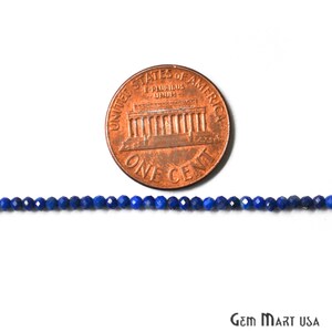 May include: A strand of dark blue lapis lazuli beads, approximately 2mm in diameter, laid out next to a US penny for size comparison. The beads are faceted and have a shiny finish.
