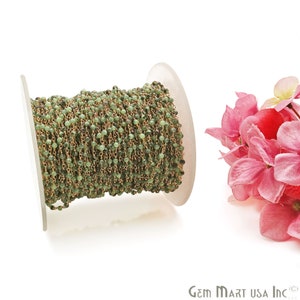 May include: A spool of green gemstone beads and gold chain, perfect for making jewelry. The beads are small and round, and the chain is delicate. The spool is white and has a label that says "Gem Mart USA Inc."